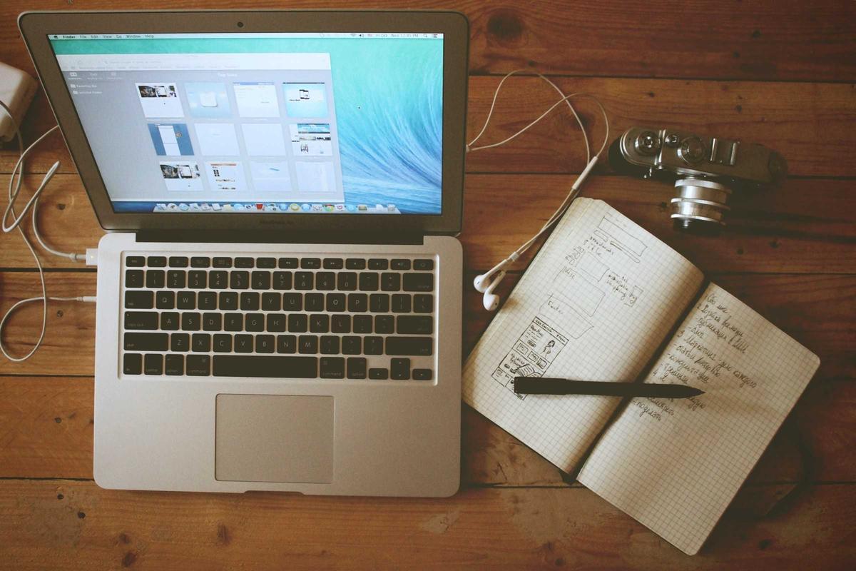 Laptop deschis pe un site, lângă un caiet cu schițe de pagini